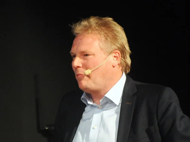 Jörgen Lennartsson med headsetmikrofon och mörk kavaj under ett föredrag på scen