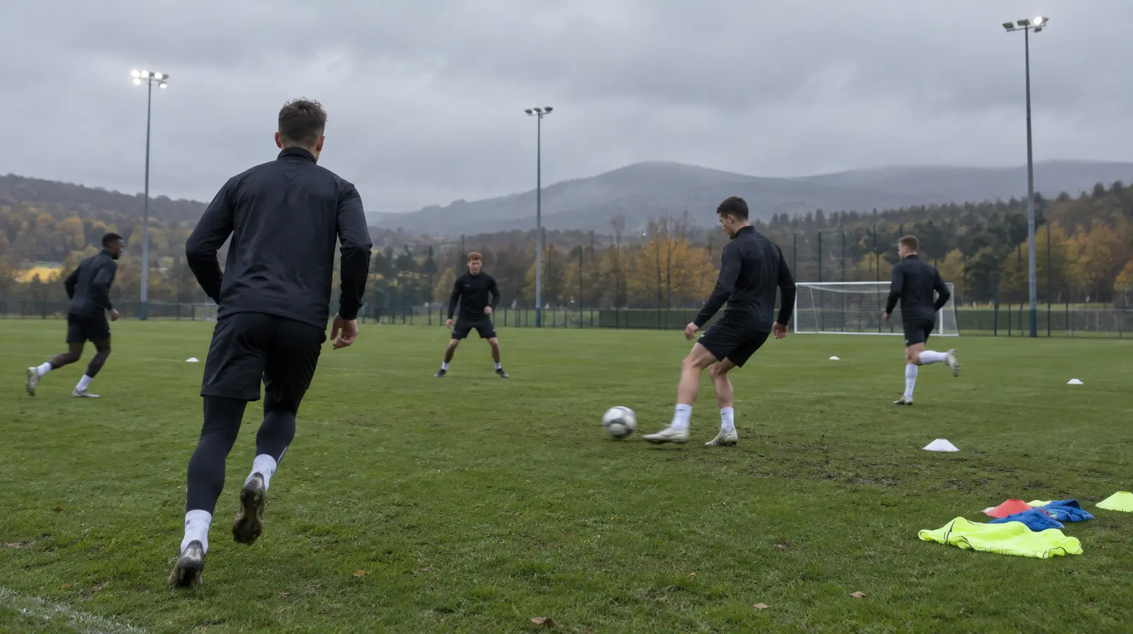 Spelare i träningskläder genomför en passningsövning på en fotbollsplan en grå morgon