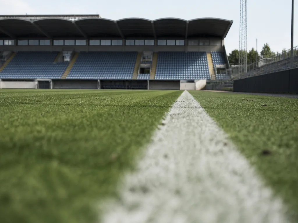 Vitmålad sidlinje på en fotbollsplan sedd i markperspektiv med gräs i solljus
